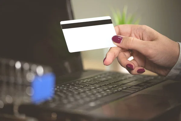 A woman buys goods in online store. Female hands is holding a credit card on a laptop background.
