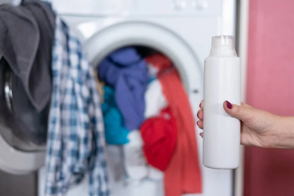 Woman is holding in hands a liquid laundry detergent on a washing machine background.