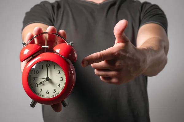 Man with red alarm clock in hand on gray background.
