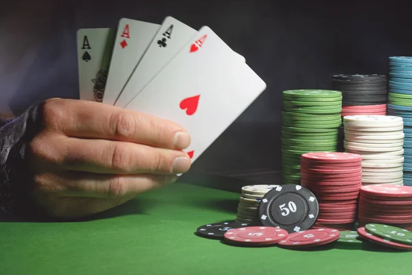 Male hand with four aces cards and poker chips on the green table background.