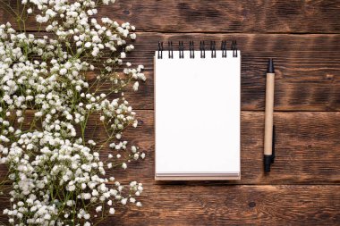 Boş sayfa not defteri, kalem ve çigila çiçeği kahverengi ahşap masa arkasında..