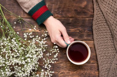 Ahşap masa arkasında bir fincan sıcak çay ve süveter giymiş kadın elleri..