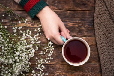 Ahşap masa arkasında bir fincan sıcak çay ve süveter giymiş kadın elleri..