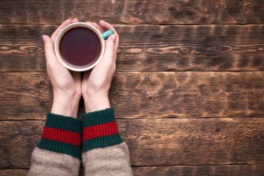 Süveter giymiş kadın elleri ve ahşap masa arkasında fotokopi alanı olan bir fincan çay..