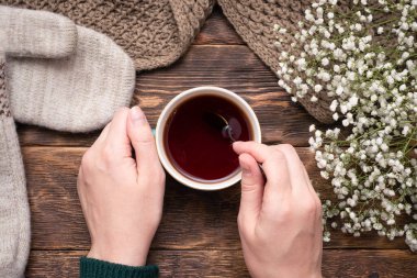 Ahşap masa arkasında bir fincan sıcak çay ve süveter giymiş kadın elleri..