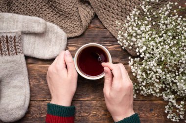 Ahşap masa arkasında bir fincan sıcak çay ve süveter giymiş kadın elleri..