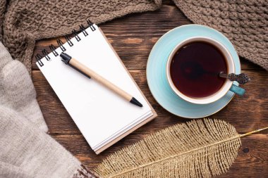 Boş sayfa defteri, kalem, sıcak çay fincanı, sıcak kıyafetler ve kahverengi ahşap masa üzerinde altın yaprak düz zemin.