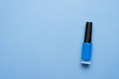 Mavi arka planda mavi tırnak cilası şişesi ve kopyalama alanı.