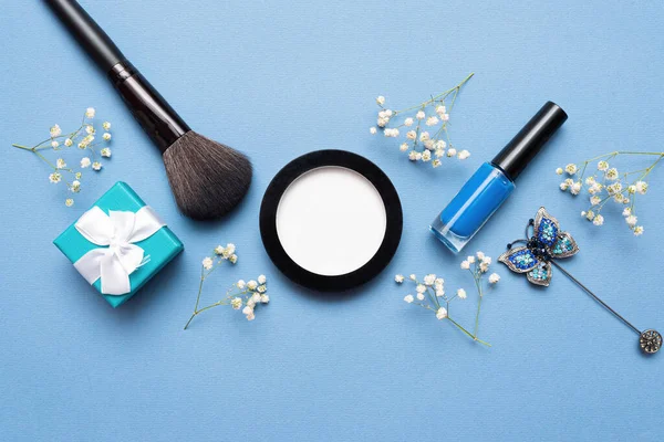 Nail polish, make up brush and gift box on blue flat lay background.