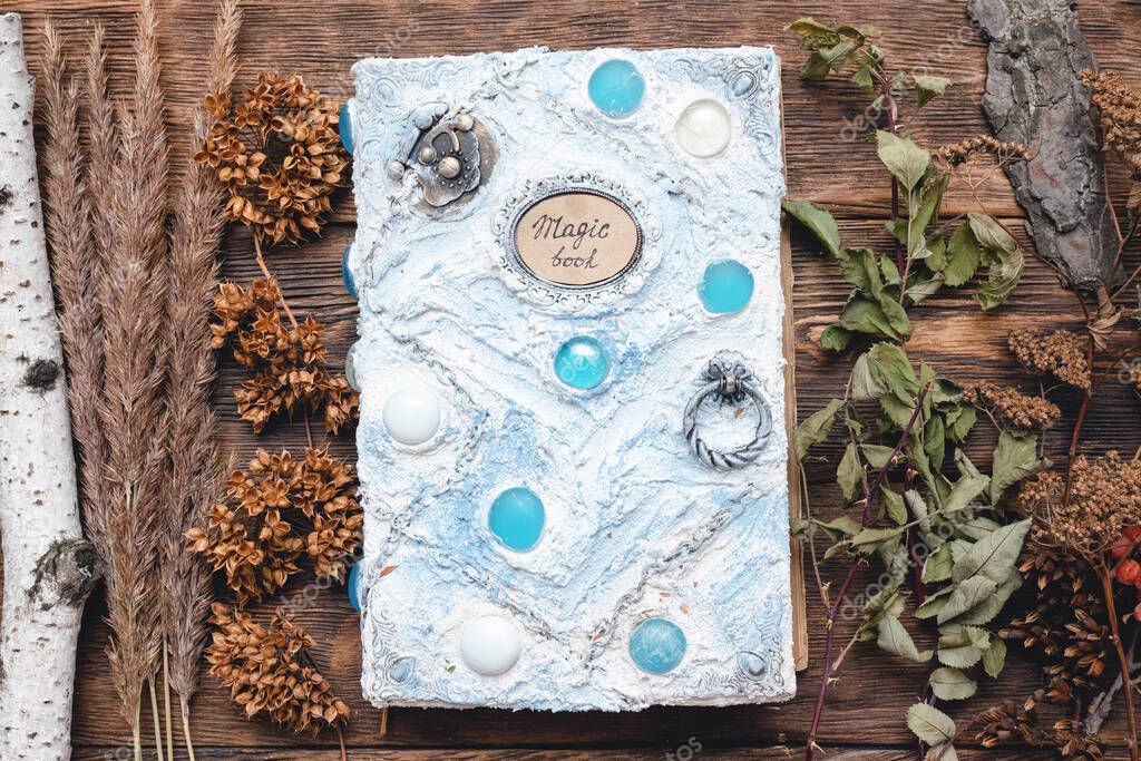 Book of magic and dried herbs on wooden table background.