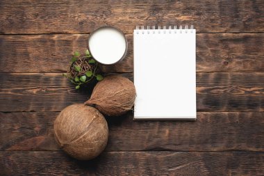 Hindistan cevizi sütü ve hindistan cevizi ve kahverengi tahta masa arkaplanının üzerinde kopya alanı olan boş sayfa defteri..