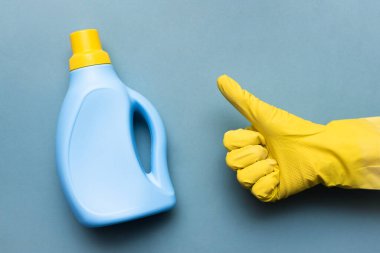 Deterjan şişesi ve eldiven mavi arka planda baş parmak işareti gösteriyor..