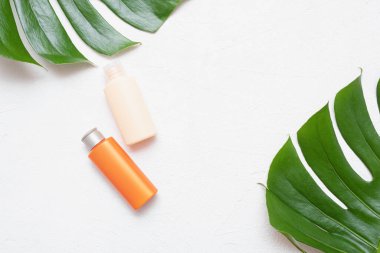 Güneş kremi ya da güneş kremi şişesi ve yeşil yaprak üzerinde fotokopi alanı olan beyaz arkaplan.