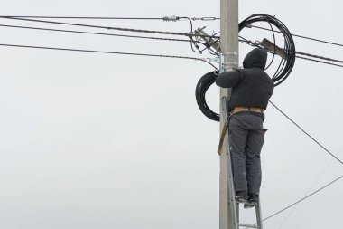 Elektrikçi dışarıdaki bir elektrik direğine yeni bir elektrik kablosu döşemiş..