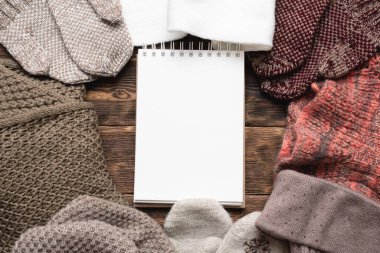 Boş not defteri ve kahverengi ahşap masa arkasında kışlık giysiler. Yapılacaklar listesi hazırlansın.