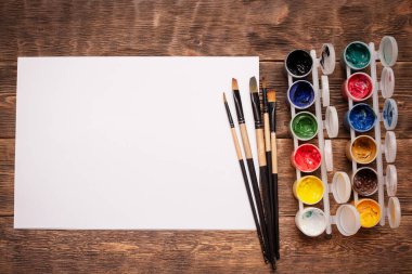 Fotokopi alanı, gouache kavanozları ve boya masası arka planında boya fırçaları olan boş beyaz sayfa.