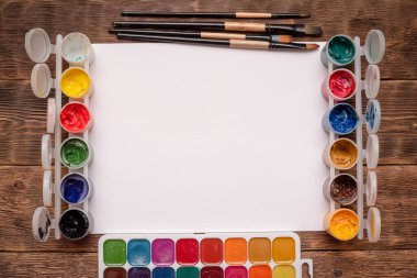 Fotokopi alanı, gouache kavanozları ve boya masası arka planında boya fırçaları olan boş beyaz sayfa.