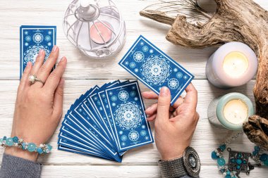 Falcı kadın ve beyaz ahşap masa üzerinde mavi tarot kartları..