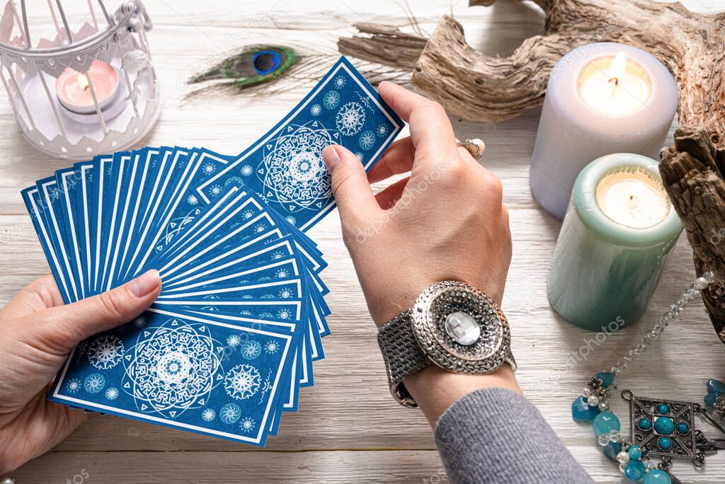 Fortune teller woman and a blue tarot cards over white wooden table background.