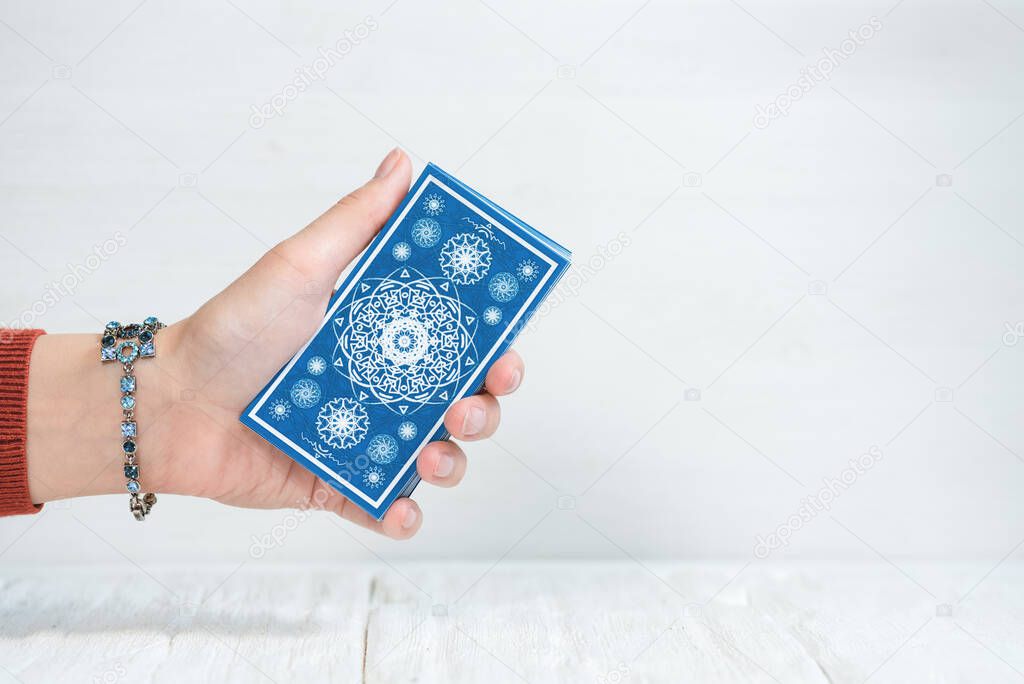 Tarot cards in fortune teller hand on white wooden table background. Future reading.