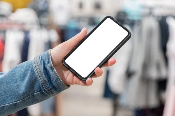 A mobile phone with blank screen in buyer hand close up on a clothing store background.
