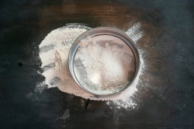 Ahşap mutfak masasının arka planındaki süzgeçte un var..