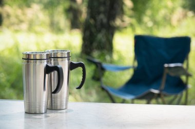 Yeşil orman arka planındaki masanın üzerinde çelik bir turist kupası..