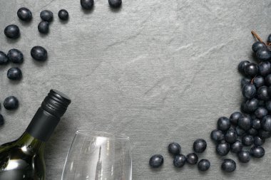 Taş masadaki şarap kadehi, şişe ve siyah üzümler düz zemin üzerinde yatıyordu..