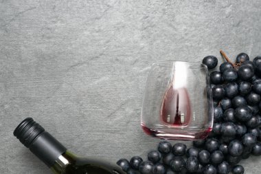 Taş masadaki şarap kadehi, şişe ve siyah üzümler düz zemin üzerinde yatıyordu..