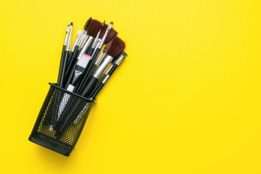 Sarı düz arkaplandaki çeşitli siyah makyaj fırçaları kopya alanı ile yatıyordu.