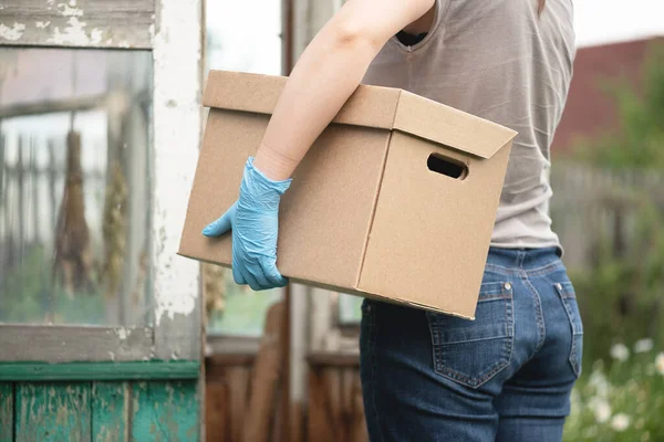 Courier in medical gloves with a cardboard box in hands close up.