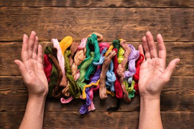 Kahverengi masa arkaplanındaki kadın ellerinde renkli nakış iplikleri.