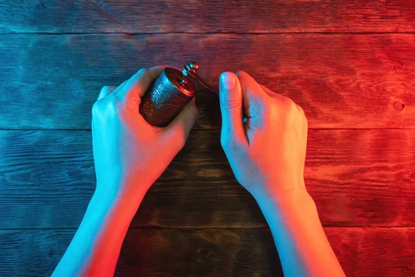 Small pepper mill in female hands in the neon light background.