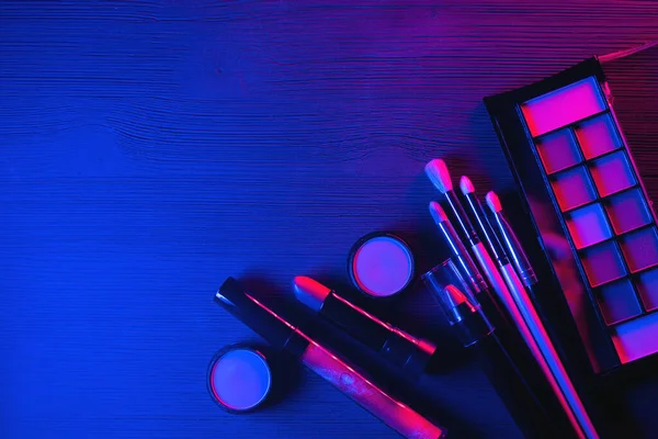 Eyeshadows palette, lipstick and makeup brushes in the neon lights background with copy space.