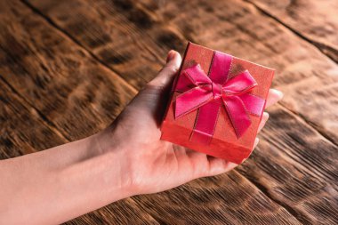 Küçük kırmızı bir hediye kutusu, arka plandaki tahta masada kadınların elinde..