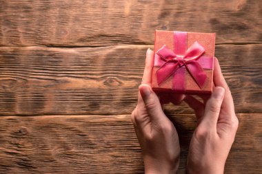 Küçük kırmızı bir hediye kutusu. Kadın ellerinde. Ahşap masa zemininde fotokopi alanı var..