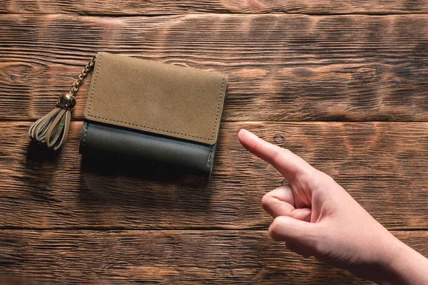Woman is showing by her index finger on the wallet on the table.
