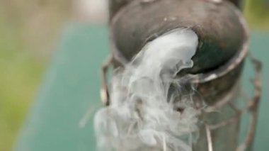 Tütsühane ve sigara içen kişi, bal için çerçeveyle birlikte bir kovanın üzerinde duruyor. Arıcılık ve arıcılık teması.