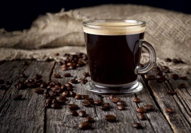 Ahşap arka plan üzerinde kahve çekirdekleri ile cam fincan kahve. 