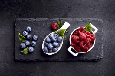 Siyah arka plan üzerine beyaz kase taze olgunlaşmış meyve. Ahududu ve yaban mersini siyah taş.