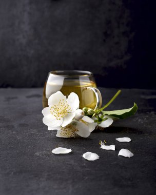 Yasemin çiçekleri ve siyah bir arka plan üzerinde sağlıklı çay fincan. H