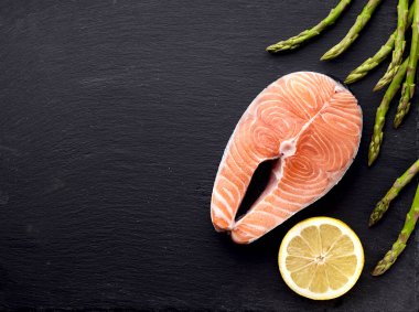 Siyah arka planda kuşkonmaz ve limonlu somon balığı. Siyah arka planda biftek. Üst görünüm.