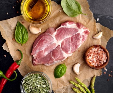 Siyah taşın üzerinde et, biberiye, fesleğen. Biber, kuşkonmaz ve zeytinyağı. Baharatlı biftek. Üst görünüm.