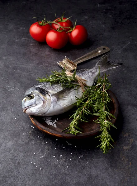 Siyah zemin üzerinde ahşap tabakta biberiye ve domatesli Dorado balığı..