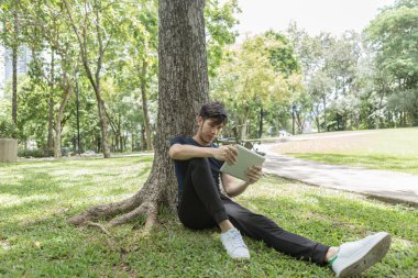 Genç iş adamı kullanımı tablet ve eğilerek parkta ağaç üzerinde.