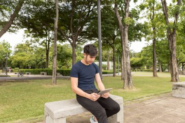 Genç iş adamı tableti kullanmak ve park sandalyede oturmak.
