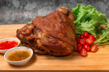 Pork knuckle or German pork hocks with vegetable and fruit served with sauce on chopping board and on wooden table. clipart