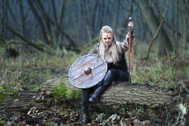 Sarışın Kuzey savaşçı kadını ile kalkan ormandaki ve elinde kılıç kanla kaplı. Bir oturum açma savaş sonrası istirahat Viking kadın.