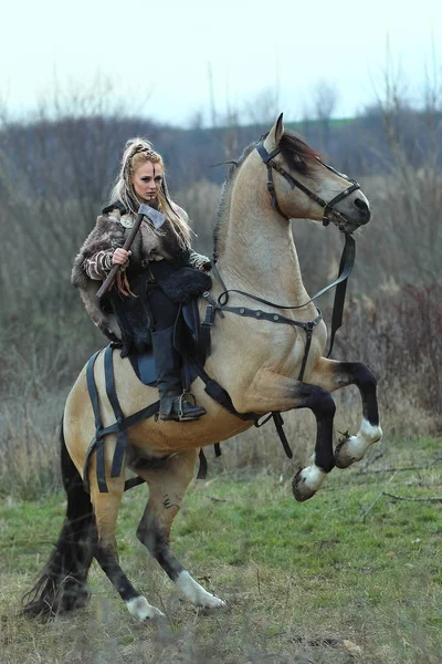Sarışın Viking savaşçı kadını elinde balta ile bir binicilik. İskandinav savaşçı kadını ormanda savaş makyaj, saldırmaya hazır ile