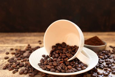 Portafilter arka planda kahve ile masada beyaz kupa kavrulmuş kahve çekirdekleri.